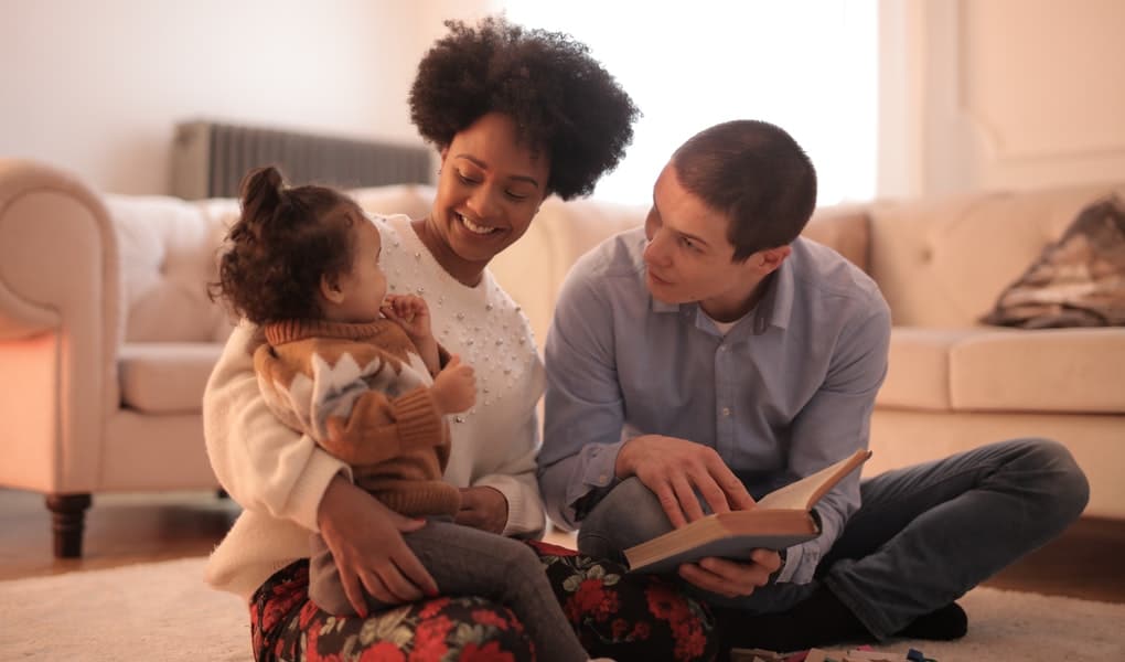 mladá inetrkultúrna rodinka si užíva zábavu pri spoločnom čítaní malej dcérke knižky 