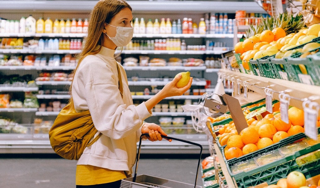 mladá žena v žltom tričku a bielej bunde nakupuje ovocie s rúškom na tvári počas covid 19